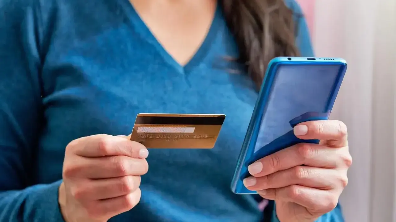 Kobieta trzyma kartę i telefon, planując jak przelać pieniadze z Revoluta.