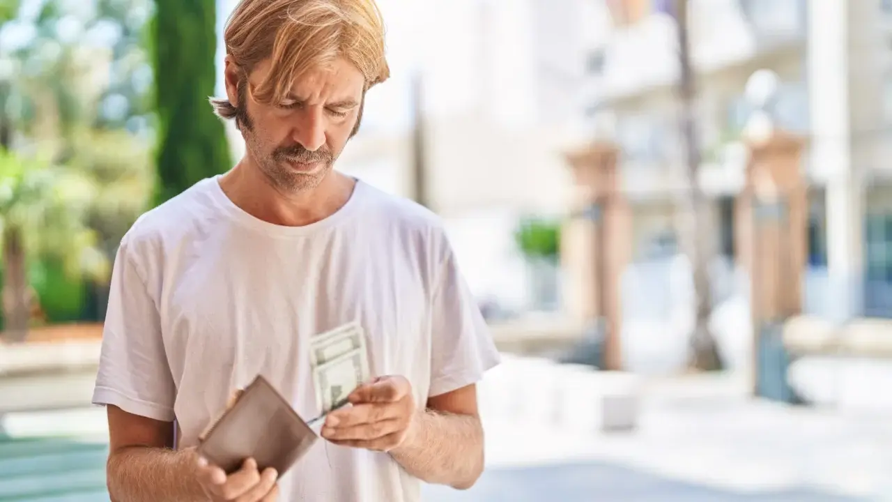 Mężczyzna z wąsami i blond włosami przegląda pieniądze w portfelu. Zastanawia się, co to jest loonheffing, gdy widzi banknoty.