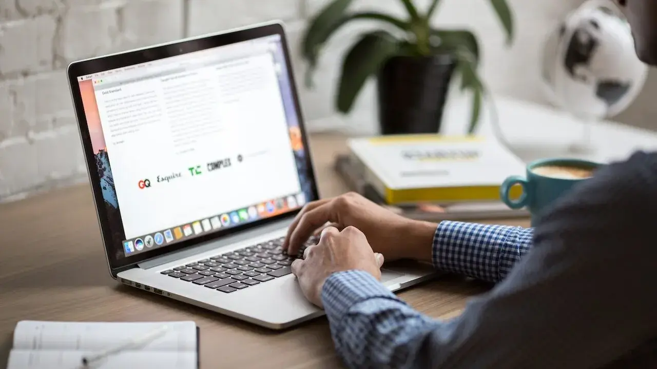 Osoba pracuje na laptopie, szukając informacji o zwrot podatku z Norwegii kiedy. Na biurku kawa i książki.