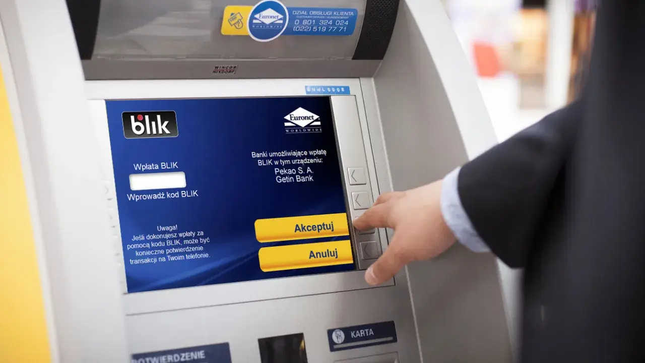 Mężczyzna używa bankomatu do wypłaty pieniędzy telefonem BLIK. Na ekranie widnieje instrukcja "Wprowadź kod BLIK".