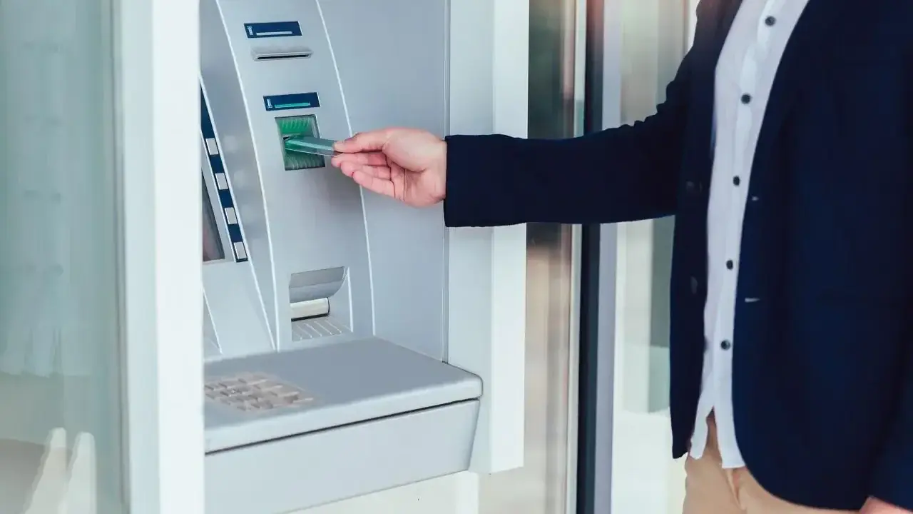 Mężczyzna wkłada kartę do wpłatomatu, który przyjmuje różne banknoty.