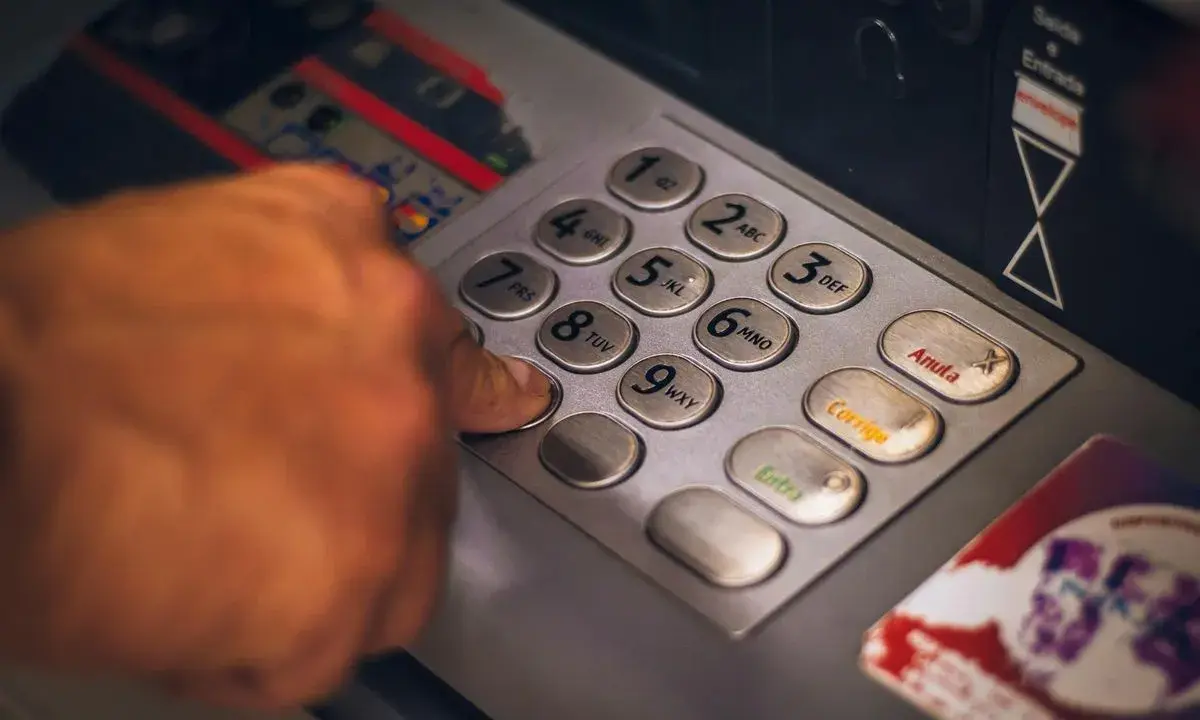 Dłoń naciska klawisz bankomatu, przygotowując się do transakcji. Szybko i sprawnie jak wypłacić czek blik z bankomatu.
