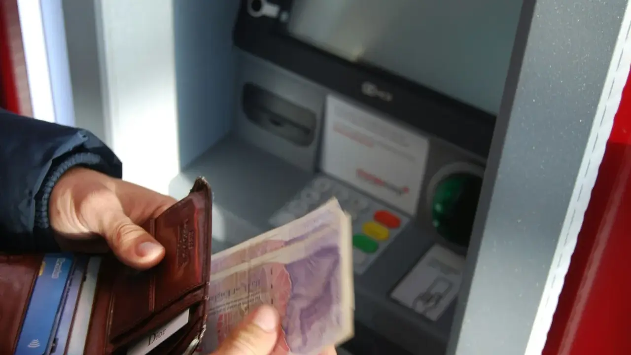 Ręce trzymają portfel i banknoty przy bankomacie. Czy da się wyplacic pieniadze bez karty? Tak, jeśli masz kod PIN.