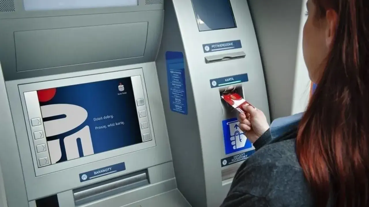 Kobieta wkłada kartę do bankomatu Banku Millennium. Ekran wyświetla powitanie.