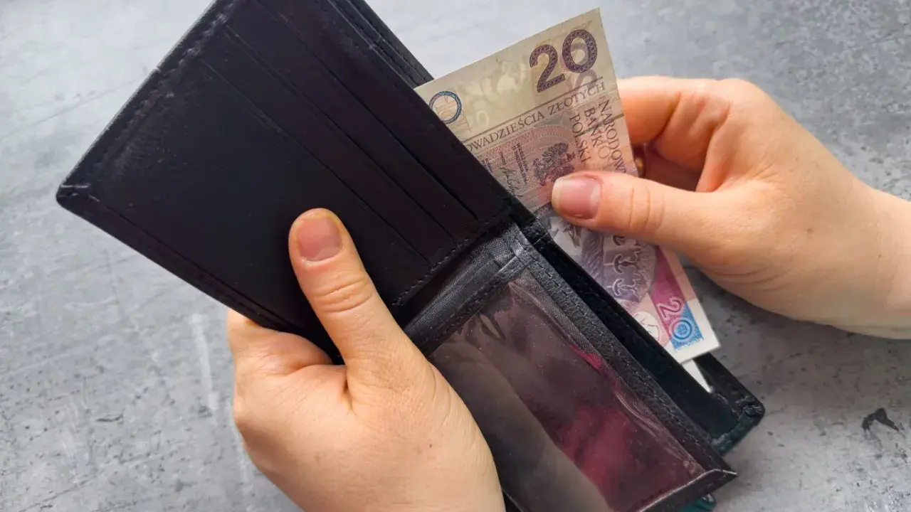 Dłonie wkładają banknot 20 zł do portfela. Czekasz na zasiłek dla bezrobotnych?