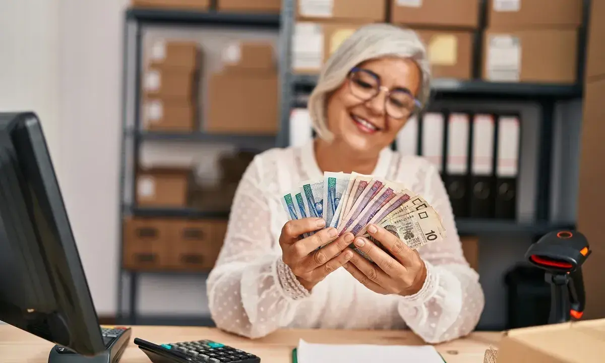 Uśmiechnięta kobieta liczy pieniądze, zastanawiając się, jaka emerytura przy zarobkach 5000 brutto.