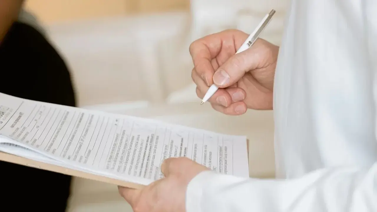 Ręka trzymająca długopis nad dokumentami. Widać fragmenty formularzy, które mogą być związane z Familienkasse druki po polsku.