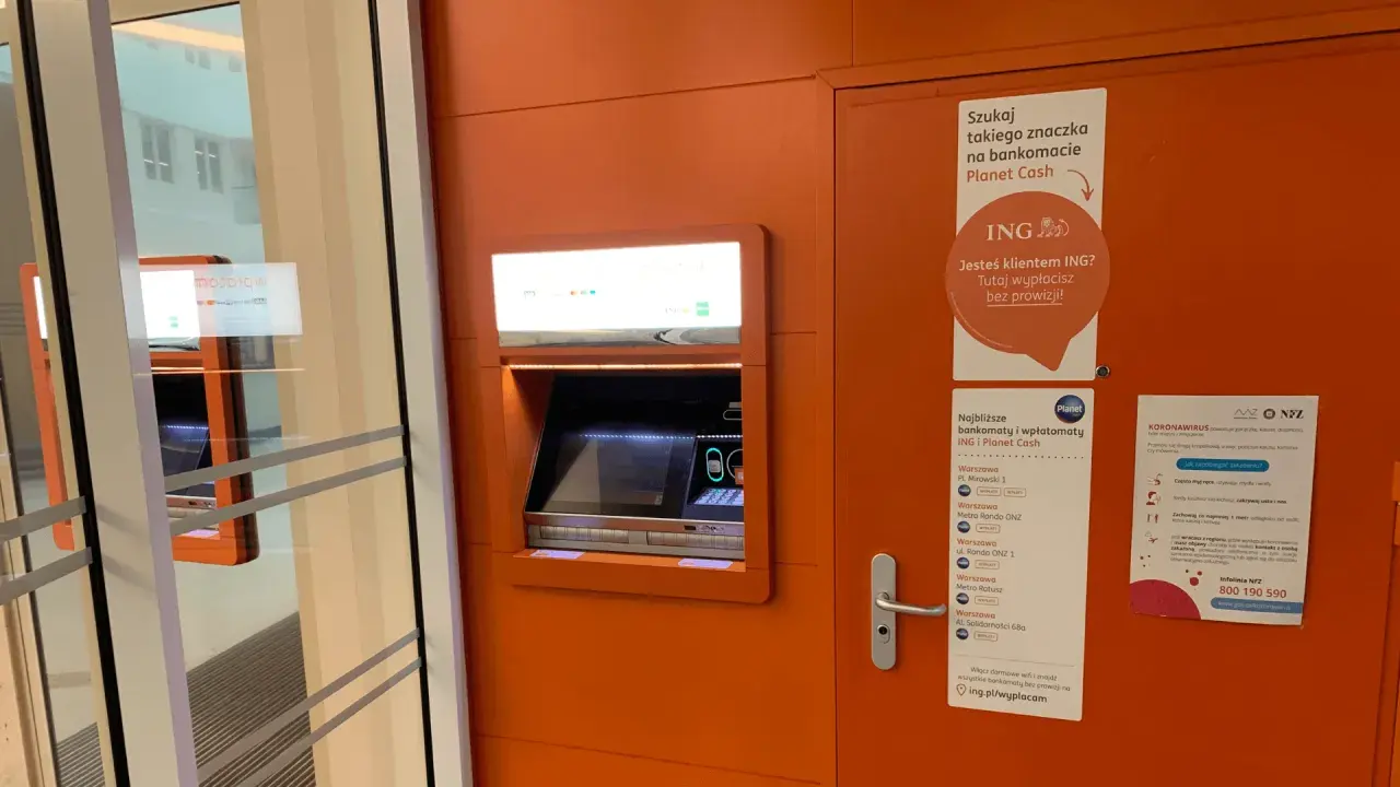 Bankomat Planet Cash z informacją o braku prowizji dla klientów ING. W pobliżu znajduje się też plakat o koronawirusie.