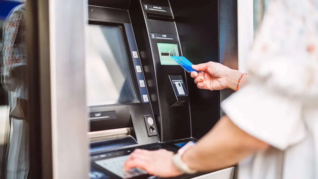 Kobieta wkłada kartę do bankomatu PKO, aby dokonać wypłaty gotówki.
