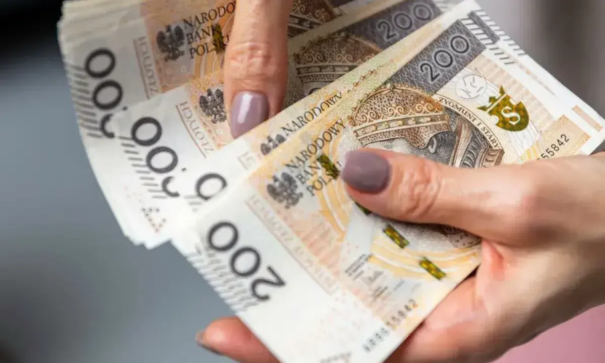 Dłonie trzymające polskie banknoty 200 zł. Czy można pobierać 500 plus i Kindergeld?