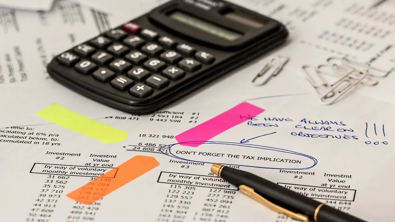 Kalkulator, dokumenty i karteczki samoprzylepne wskazują na analizę finansową, być może dotyczącą kwoty wolnej od podatku w Niemczech.