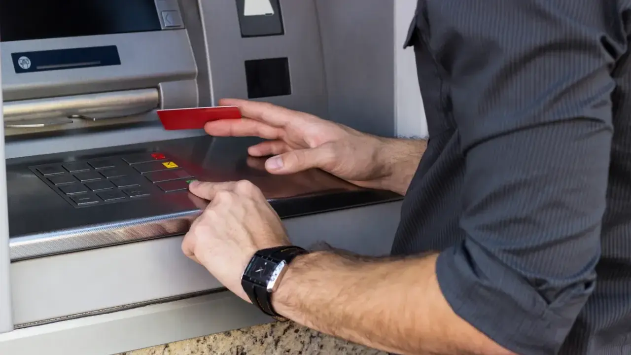 Mężczyzna wkłada kartę do bankomatu, przygotowując się, jak wypłacić pieniądze z bankomatu za granicą.
