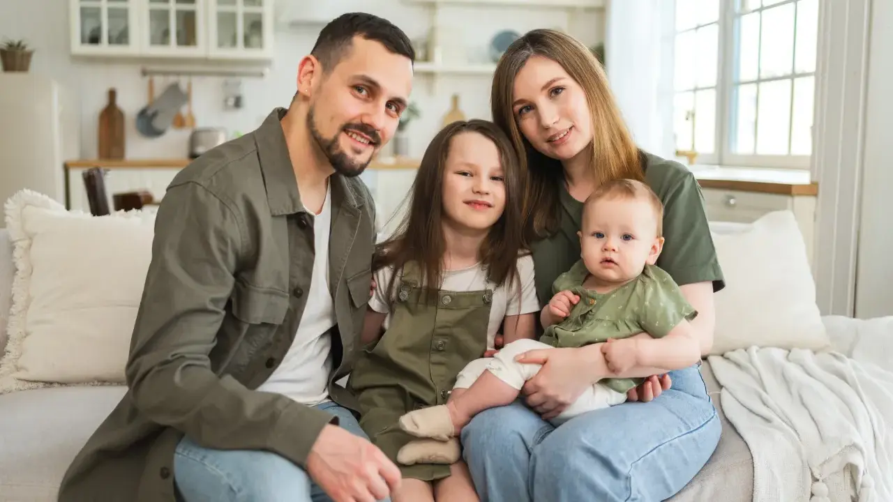 Szczęśliwa rodzina na kanapie. Rodzice z dwójką dzieci, starszą córką i niemowlęciem. Myślą o przyszłości i wsparciu, jak kindergeld po 18 roku życia.
