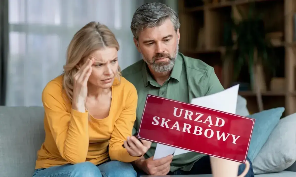 Para zmartwiona analizuje dokumenty, trzymając tabliczkę "Urząd Skarbowy". Rozważają wspólne rozliczenie bez ślubu.