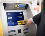 Mężczyzna używa bankomatu do wypłaty pieniędzy telefonem BLIK. Na ekranie widnieje instrukcja "Wprowadź kod BLIK".