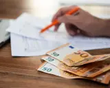 Rozłąkowe w Niemczech: stos 50 euro na biurku, ręka z długopisem nad dokumentami.