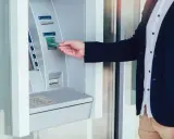 Mężczyzna wkłada kartę do wpłatomatu, który przyjmuje różne banknoty.