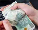 Ręce trzymające stos banknotów 100 zł na tle klawiatury laptopa. Czy w Żabce można wpłacić pieniądze?