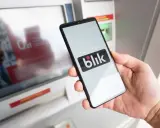 Dłoń trzyma smartfon z logo Blik przed bankomatem. Czy można wpłacić pieniądze Blikiem? Ta technologia ułatwia transakcje.