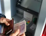 Ręce trzymają portfel i banknoty przy bankomacie. Czy da się wyplacic pieniadze bez karty? Tak, jeśli masz kod PIN.