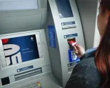 Kobieta wkłada kartę do bankomatu Banku Millennium. Ekran wyświetla powitanie.
