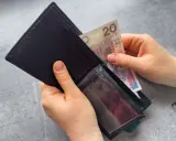 Dłonie wkładają banknot 20 zł do portfela. Czekasz na zasiłek dla bezrobotnych?
