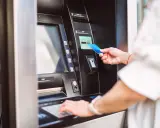 Kobieta wkłada kartę do bankomatu PKO, aby dokonać wypłaty gotówki.