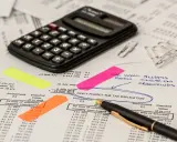 Kalkulator, dokumenty i karteczki samoprzylepne wskazują na analizę finansową, być może dotyczącą kwoty wolnej od podatku w Niemczech.