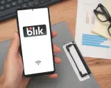 Dłoń trzyma smartfon z logo Blik. Widoczny symbol Wi-Fi sugeruje, że blik przelew na telefon nie doszedł.
