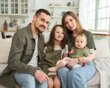 Szczęśliwa rodzina na kanapie. Rodzice z dwójką dzieci, starszą córką i niemowlęciem. Myślą o przyszłości i wsparciu, jak kindergeld po 18 roku życia.