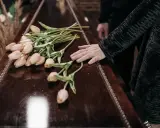 Dłoń na trumnie z tulipanami. W Niemczech zasiłek pogrzebowy może pomóc w pokryciu kosztów.