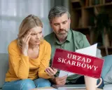 Para zmartwiona analizuje dokumenty, trzymając tabliczkę "Urząd Skarbowy". Rozważają wspólne rozliczenie bez ślubu.