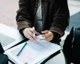 Osoba analizuje dokumenty, przygotowując się do rozliczenia podatków w Niemczech dla Polaków. Obok laptop i plecak.