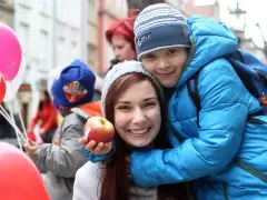 Uśmiechnięta kobieta z jabłkiem i chłopiec w niebieskiej kurtce, otoczeni balonami. To obraz kapitału opiekuńczego, pełen radości i bliskości.