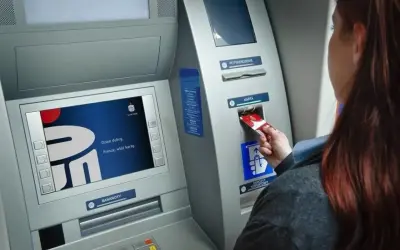 Kobieta wkłada kartę do bankomatu Banku Millennium. Ekran wyświetla powitanie.
