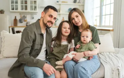 Szczęśliwa rodzina na kanapie. Rodzice z dwójką dzieci, starszą córką i niemowlęciem. Myślą o przyszłości i wsparciu, jak kindergeld po 18 roku życia.