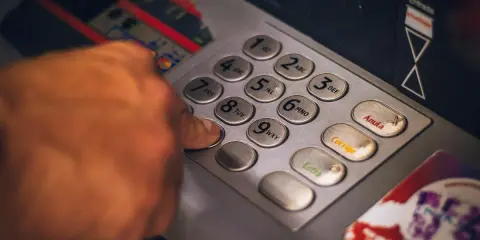 Dłoń naciska klawisz bankomatu, przygotowując się do transakcji. Szybko i sprawnie jak wypłacić czek blik z bankomatu.