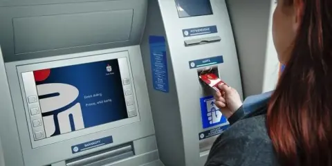 Kobieta wkłada kartę do bankomatu Banku Millennium. Ekran wyświetla powitanie.