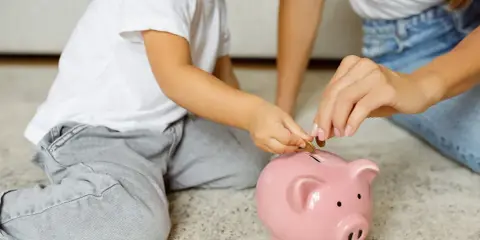 Dziecko i mama wrzucają monety do różowej świnki-skarbonki. Uczą się oszczędzać, by wiedzieć, kto wypłaca rodzinne.