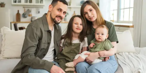 Szczęśliwa rodzina na kanapie. Rodzice z dwójką dzieci, starszą córką i niemowlęciem. Myślą o przyszłości i wsparciu, jak kindergeld po 18 roku życia.
