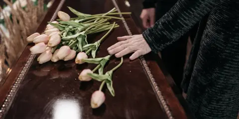 Dłoń na trumnie z tulipanami. W Niemczech zasiłek pogrzebowy może pomóc w pokryciu kosztów.