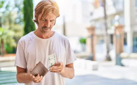 Mężczyzna z wąsami i blond włosami przegląda pieniądze w portfelu. Zastanawia się, co to jest loonheffing, gdy widzi banknoty.