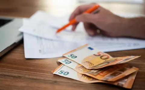 Rozłąkowe w Niemczech: stos 50 euro na biurku, ręka z długopisem nad dokumentami.