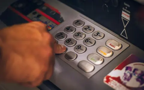 Dłoń naciska klawisz bankomatu, przygotowując się do transakcji. Szybko i sprawnie jak wypłacić czek blik z bankomatu.