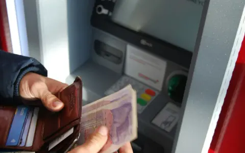 Ręce trzymają portfel i banknoty przy bankomacie. Czy da się wyplacic pieniadze bez karty? Tak, jeśli masz kod PIN.