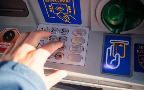 Dłoń wpisuje PIN na bankomacie. Co zrobić, gdy bankomat wciągnął kartę i jak załatwić zwrot?