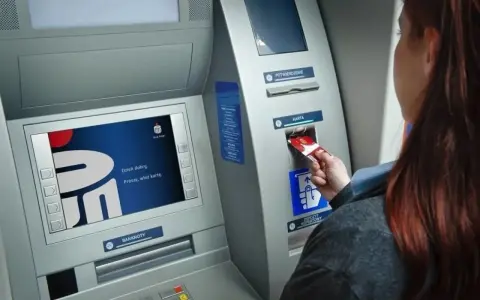 Kobieta wkłada kartę do bankomatu Banku Millennium. Ekran wyświetla powitanie.