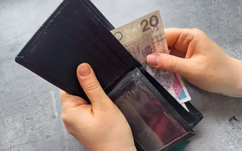 Dłonie wkładają banknot 20 zł do portfela. Czekasz na zasiłek dla bezrobotnych?