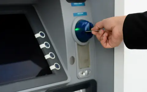 Dłoń wkłada kartę do bankomatu, próbując uzyskać dostęp do środków, ale konto bankowe jest zablokowane.