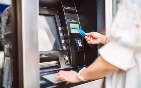 Kobieta wkłada kartę do bankomatu PKO, aby dokonać wypłaty gotówki.